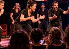 Bildbeschreibung: Redaktionelle Visualisierung zum historischen MOMENT!-Festival 2011 im TAG und Theater Drachengasse in Wien. Das Motiv zeigt das spontane Zusammenspiel eines Theaterensembles vor Publikum. Wichtiger Bildhinweis: Das Bild wurde mit künstlicher Intelligenz erstellt. Es zeigt keine Originalaufnahme des Festivals 2011, keine tatsächlichen Aufführungen und keine nachweislich beteiligten Künstlerinnen oder Künstler.